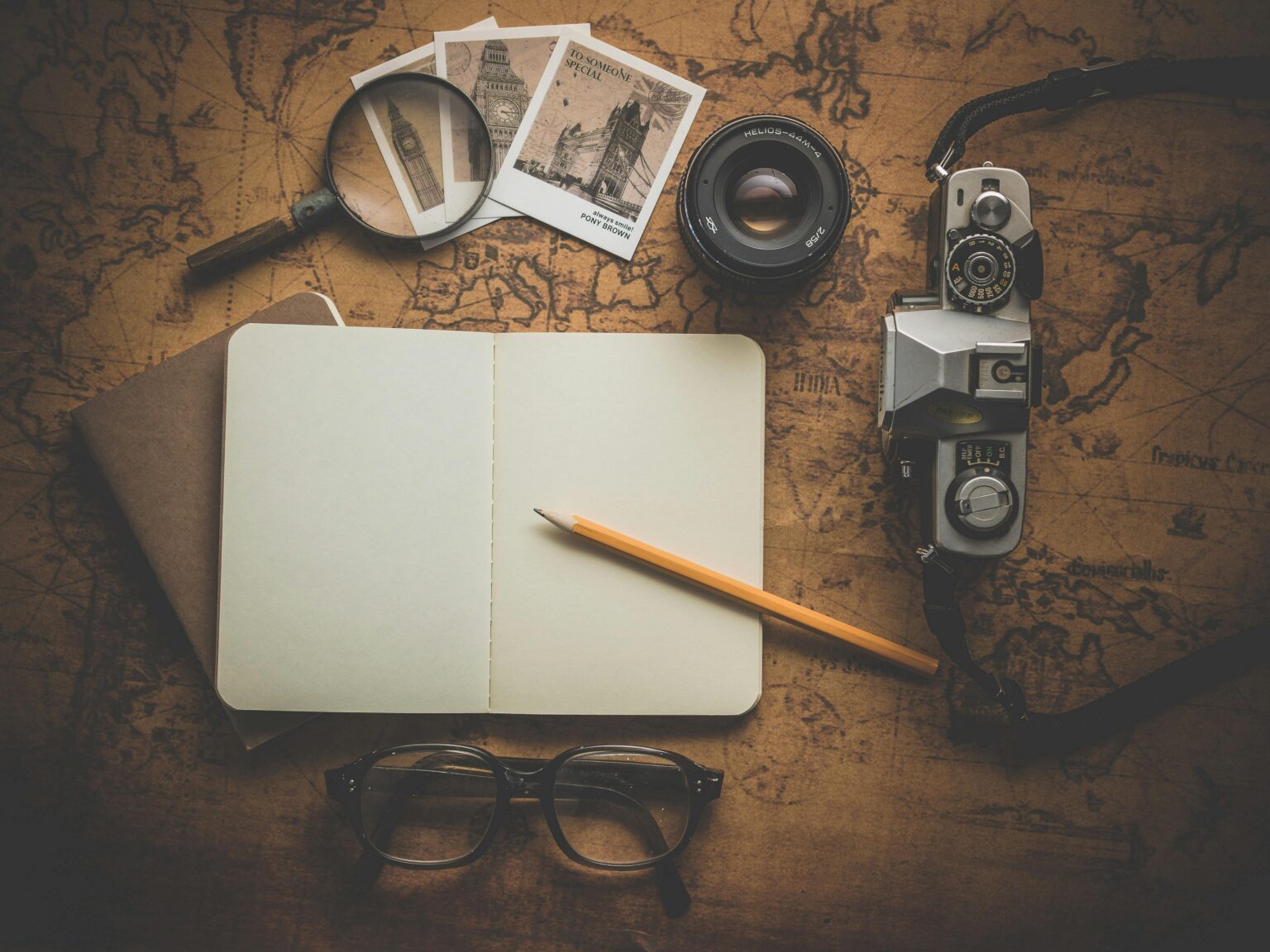 A flat lay of travel essentials on a vintage map surface, including a camera, notebook, and magnifying glass.